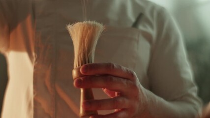 Barber dispenses shaving cream onto soft brush before procedure