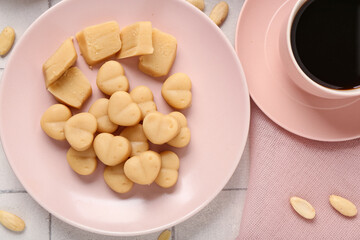 Plate with tasty marzipan candies and cup of coffee on light tile table, closeup