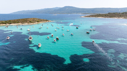 Numerous boats are anchored in the crystal clear turquoise waters of Vourvourou, Sithonia, Greece, surrounded by lush green islands, creating a picturesque summer scene © danr13