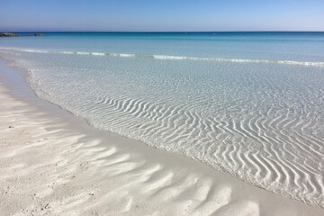 Tranquil beach with crystal-clear water.  Gentle waves create patterns in the sand
