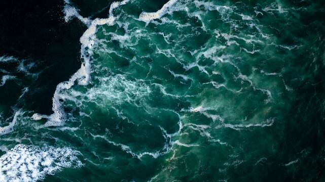 Aerial view of dark green ocean water with white splashes and foam, creating a beautiful abstract pattern