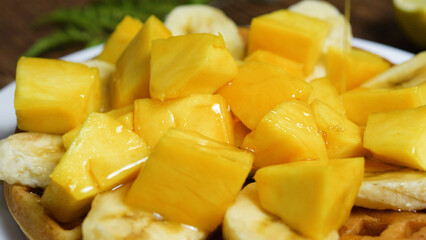 Honey pouring over freshly made waffles, topped with vibrant slices of banana and mango, creates a tempting and nutritious breakfast or brunch option bursting with flavor