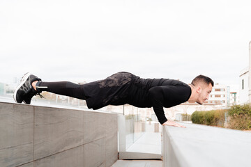 Young man doing push-ups on rooftop retaining wall