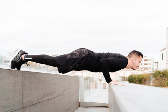 Young man doing push-ups on rooftop retaining wall