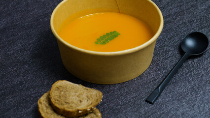 Pumpkin soup is served in an eco friendly bowl with a black spoon and slices of whole wheat bread, presenting a healthy and sustainable meal option