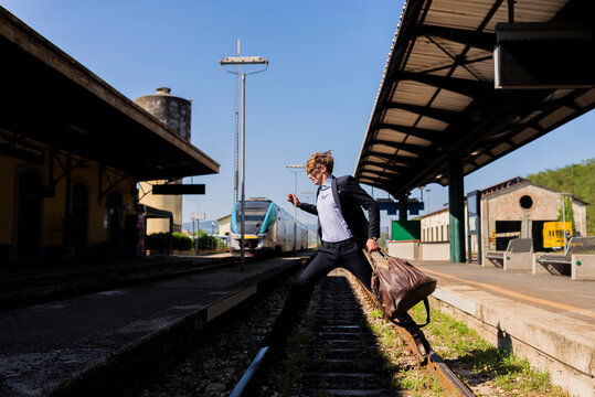 Young businessman jumping over tracks at train station
