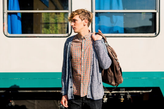 Young man with leather bag standing in front of a train