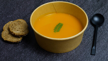 Creamy pumpkin soup nestled in biodegradable vessel, accompanied by crisp toasted bread slices, representing wholesome seasonal dining with environmental consciousness