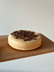 Sponge cake with chocolate chips on wooden board against white wall