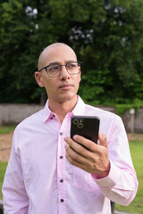 Bald Hispanic man wearing pink casual business shirt and eyeglasses outdoors while thinking