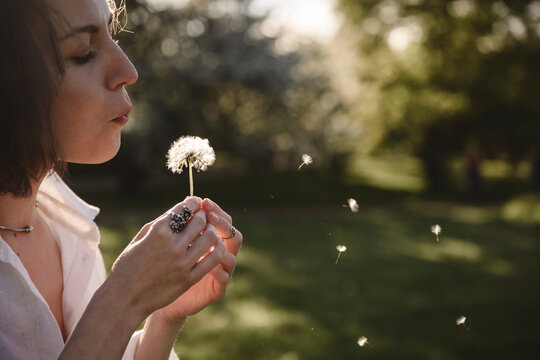 Woman blowing dandelion in the park at sunset in summer