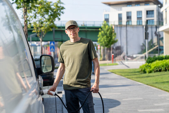 Delivery man charging electric van near sidewalk at street