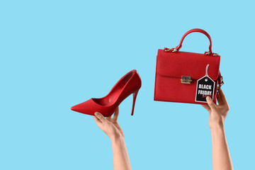 Female hands holding stylish high heels, bag and tag with text BLACK FRIDAY SALE on blue background