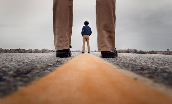 View through standing legs to a curly man standing on the medial strip of a road