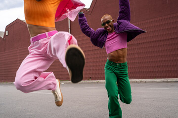 Happy non-binary person jumping with friend in front of building