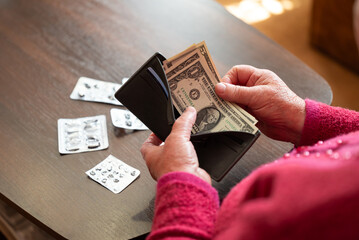 Medication needs in old age with low funds in the USA. A pensioner in the USA holds dollars in her wallet next to empty blister packs of medication, lack of access to treatment