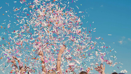 High school students joyfully celebrating graduation by tossing colorful confetti under a clear blue sky