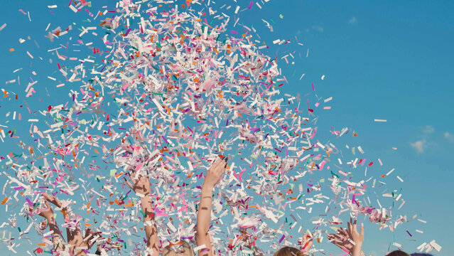High school students joyfully celebrating graduation by tossing colorful confetti under a clear blue sky