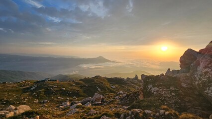 A breathtaking view of the Caucasus mountains in Dagestan at sunset. The landscape features rocky terrain, lush greenery, and a vibrant sky with clouds.