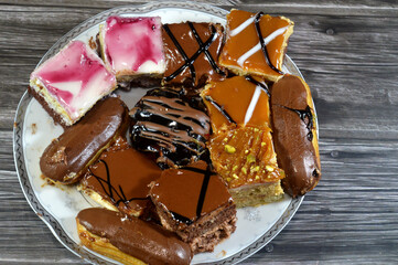 Plate of Assorted small Gateaux with different topping, Gateau bites are small bite-sized portions of cake, made of various cake flavors and fillings, miniature cakes, Eclairs, mille feuille