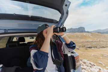 Happy woman looking through binoculars during a car trip to the mountains
