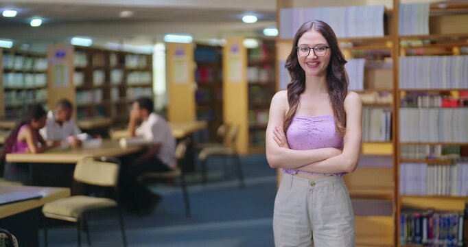 Indian asian young adult gen z lady student standing proud fold hand look camera indoor library happy smiling girl cross arm staring cam do casual pose ready for exam enjoy day time inside college
