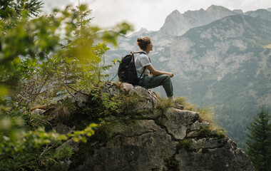 Young woman hiker relaxing sitting on rock with mountain view during trekking in nature