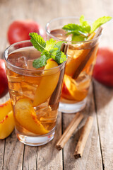 Refreshing peach iced tea in glass with ice cubes and cinnamon on wooden table