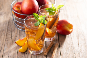 Refreshing peach iced tea in glass with ice cubes and cinnamon on wooden table