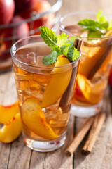 Refreshing peach iced tea in glass with ice cubes and cinnamon on wooden table