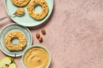 Plates with apple rounds, bowl of nut butter and hazelnuts on pink grunge background