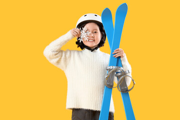 Little Asian girl with skis and snowflake on yellow background