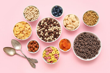 Bowls with different tasty cereals, dry fruits and nuts on pink background