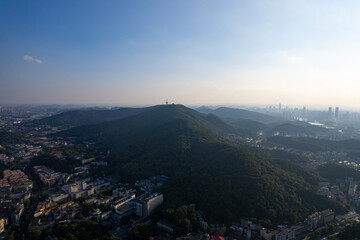 Obraz premium A sweeping aerial vista showcases a large urban city in China, with a lush green mountain towering over its modern buildings and serene landscape.