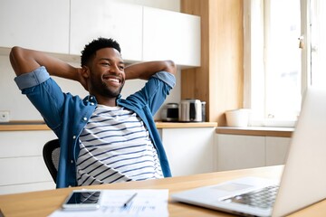 Relaxed african american man working from home on laptop in kitchen enjoying the day off