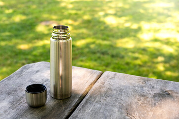 Coffee in a thermos on a wooden picnic table in the park. Copy space.