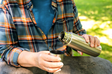 Elderly woman drinks coffee from a thermos on a picnic in the park. Relaxing and enjoying life. Summer or autumn sunny day. Close-up.