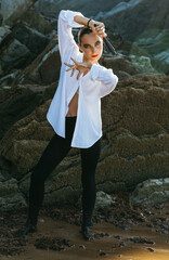 Flamenco dancer posing with fan among coastal rocks, looking at camera
