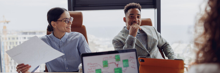 A diverse business team discusses thoughtfully, using modern technology with a city skyline view...