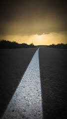 An empty road extending into the horizon amidst a natural landscape with dramatic skies, evoking a feeling of endless exploration and anticipation.