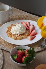 Delicious breakfast with waffles, fresh strawberries, whipped cream and coffee on a cozy table setting