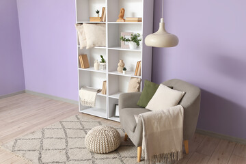 Fototapeta premium Interior of stylish living room with grey armchair, pouf and bookshelf