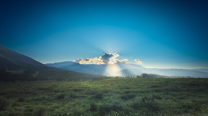 A serene landscape with a lush meadow, mountains, clear sky, and sunlight highlighting the scenery,...