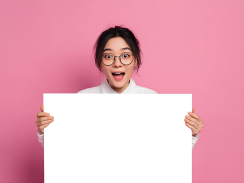 A cheerful young woman of Asian descent, her expression mirroring astonishment, poses against a vibrant pink backdrop, her hands outstretched to present a blank poster board.