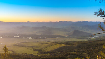 Aerial view of a valley with mountains, river, forests, and a village. Tranquil scenery with clear skies, sunrise/sunset lighting, and vibrant colors.