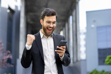 Fototapeta na wymiar Successful young professional excitedly reading news on smartphone outdoors
