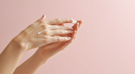 Close-up of Elegant Female Hands Applying Moisturizing Hand Cream, with a Visible Dollop of White Product and Gentle Strokes, Against a Soft Pastel Pink Background