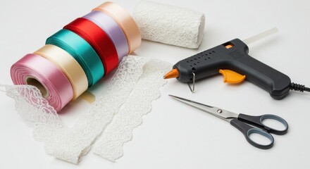 Assortment of crafting supplies laid on a white surface. Includes spools of colorful satin ribbon, lace, a glue gun, scissors, and rolled gauze