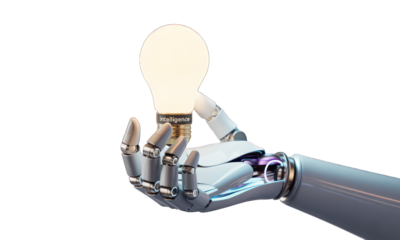 Robot hand holds a glowing lightbulb; black background, bright idea concept