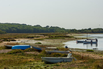 Mudeford Sandbank, Southbourne, UK - August 10th 2025: Boats left on beach, with people alongside a sailboat in the background.